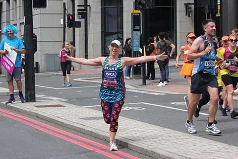 A woman wearing an RSPCA charity vest with arms outstretched at organised charity run.